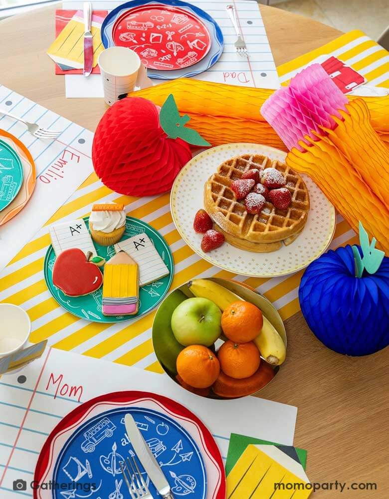 A festive back to school first day of school celebration party table setting featuring Momo Party's back to school themed party supplies including the No. 2 pencil patterned dinner plates, school day side plates with school supplies designs in different colors, and loose leaf paper placemat by Gatherings. With apple and pencil shaped honeycomb as the centerpiece, plus a plate of fruits school supply themed sugar cookies, makes a great inspo to celebrate the start of the new school year with kids!