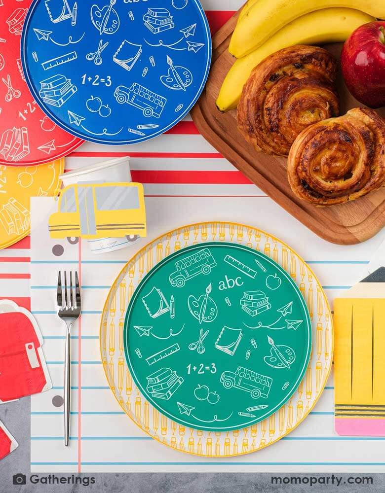 A festive back to school first day of school celebration party table setting featuring Momo Party's back to school themed party supplies including the No. 2 pencil patterned dinner plates, school day side plates with school supplies designs in four different colors, and the notebook inspired placemat by Gatherings. With pencil shaped napkins and red backpack shaped napkins, plus a plate of treats and fruits, this makes a great inspo to celebrate the start of the new school year with kids!