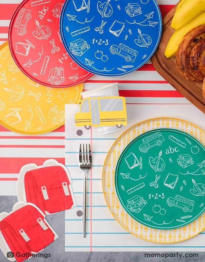 A festive back to school first day of school celebration party table setting featuring Momo Party's back to school themed party supplies including the No. 2 pencil patterned dinner plates, school day side plates with school supplies designs in four different colors, and the notebook inspired placemat by Gatherings. With pencil shaped napkins and red backpack shaped napkins, plus a plate of treats and fruits, this makes a great inspo to celebrate the start of the new school year with kids!