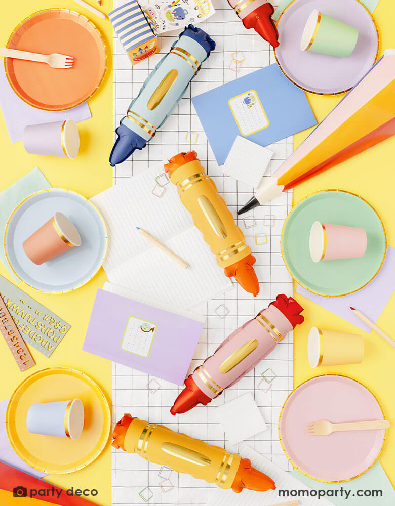 A overhead shot of a back to school party table featuring Momo Party's school themed tableware and decorations including mini crayon shaped balloon set, a black and white grid table runner, pastel colored plates and party cups and a few pastel colored stationary including notebooks, rulers, pencils etc. Making this a modern and adorable inspo for a fun back to school party or first day of school celebration. 