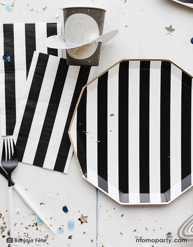 A space themed party table featuring Momo Party's Black Striped Party Supplies including paper dinner plates, guest towels, black and white cutlery set. With the planet 3D party cup and metallic star confetti around the table, this makes a perfect inspo for a chic, stylish and modern space themed celebration.