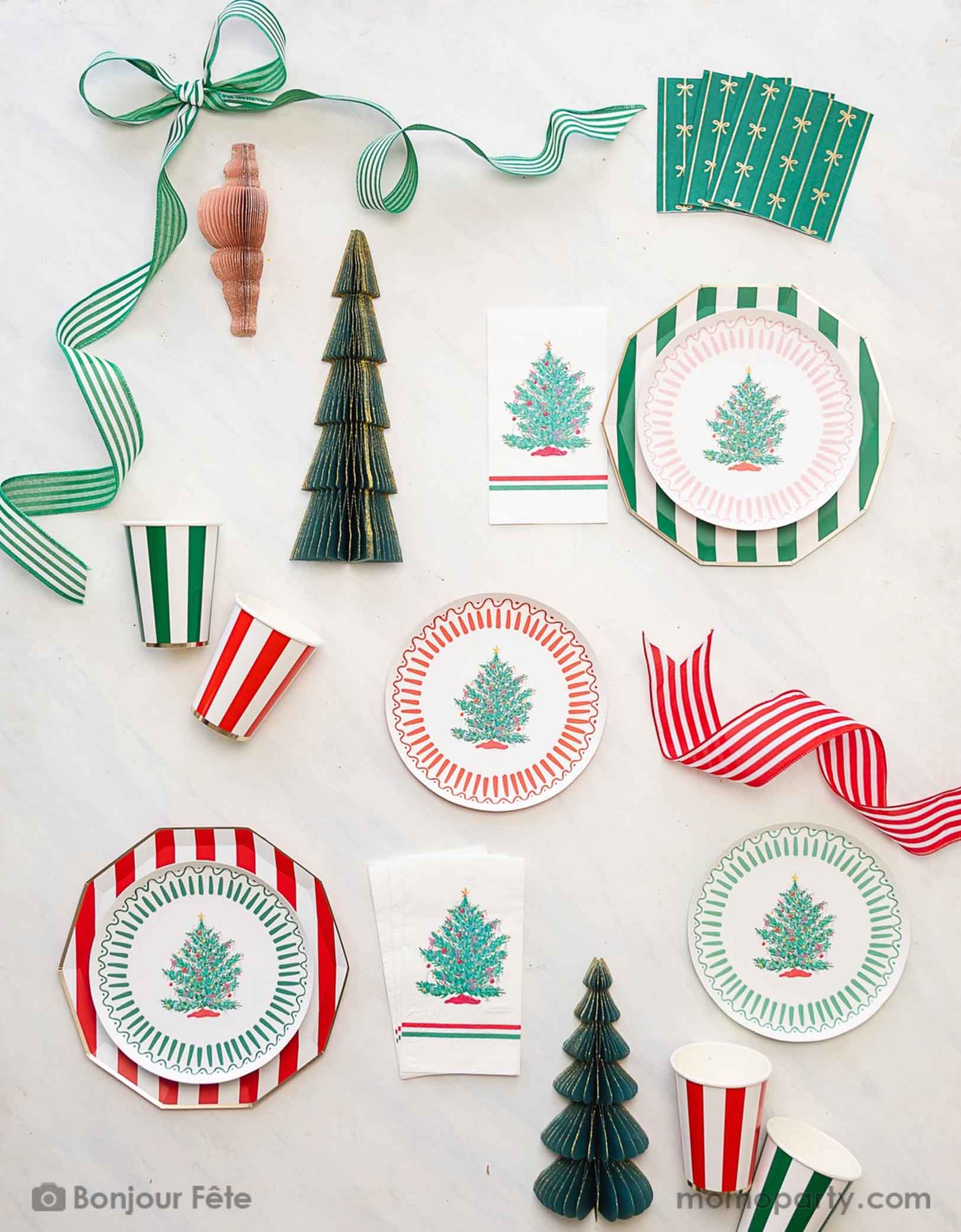 An elegant Christmas party tablescape featuring striped party tableware in red and green with bows and vintage Christmas tree illustration. A chic and modern style to celebrate the Holly Jolly holiday season.