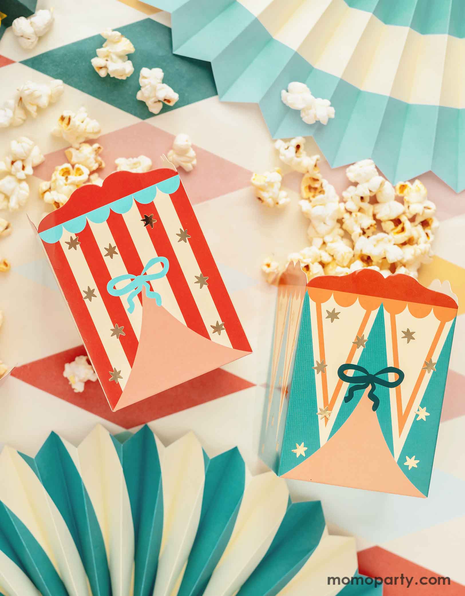 A carnival/circus themed part table featuring Momo Party's circus themed party supplies including  the festive treat boxes filled with popcorn and colorful paper fans on a circus themed striped table cover - making this great table setting idea for a fun and festive kid's carnival themed birthday celebration!