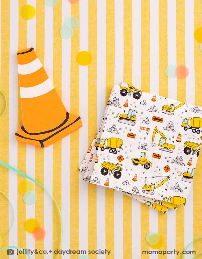 Momo Party's contruction themed paper napkins and construction cone shaped napkins by Daydream Society on a bright yellow striped tablecloth. Around the napkins are some color matching round confetti and ribbons, a cheerful additions to a kid's construction themed birthday party.