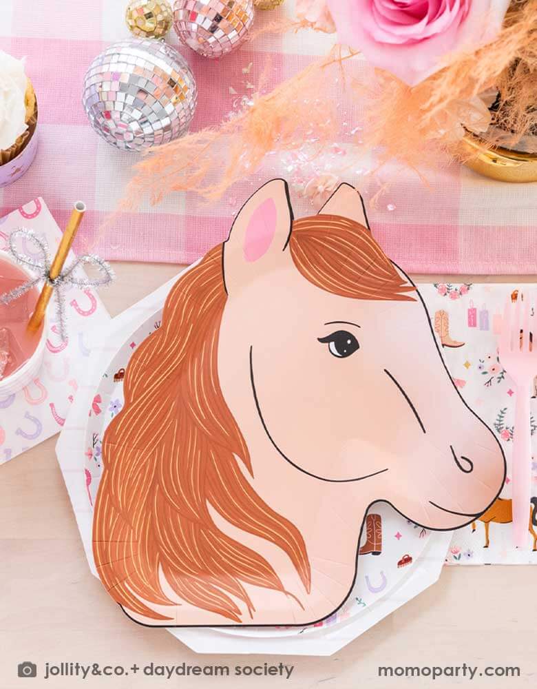 A cowgirl pony themed birthday party table featuring Momo Party's 9" x 11" pony shaped plates, cowgirl motif side plates and napkins by Daydream Society. In the middle of the party table there's a pink gingham patterned linen runner with disco ball decorations and pink flower bouquet , making this a perfect tablescape idea for a girly pony / western cowgirl themed celebration.