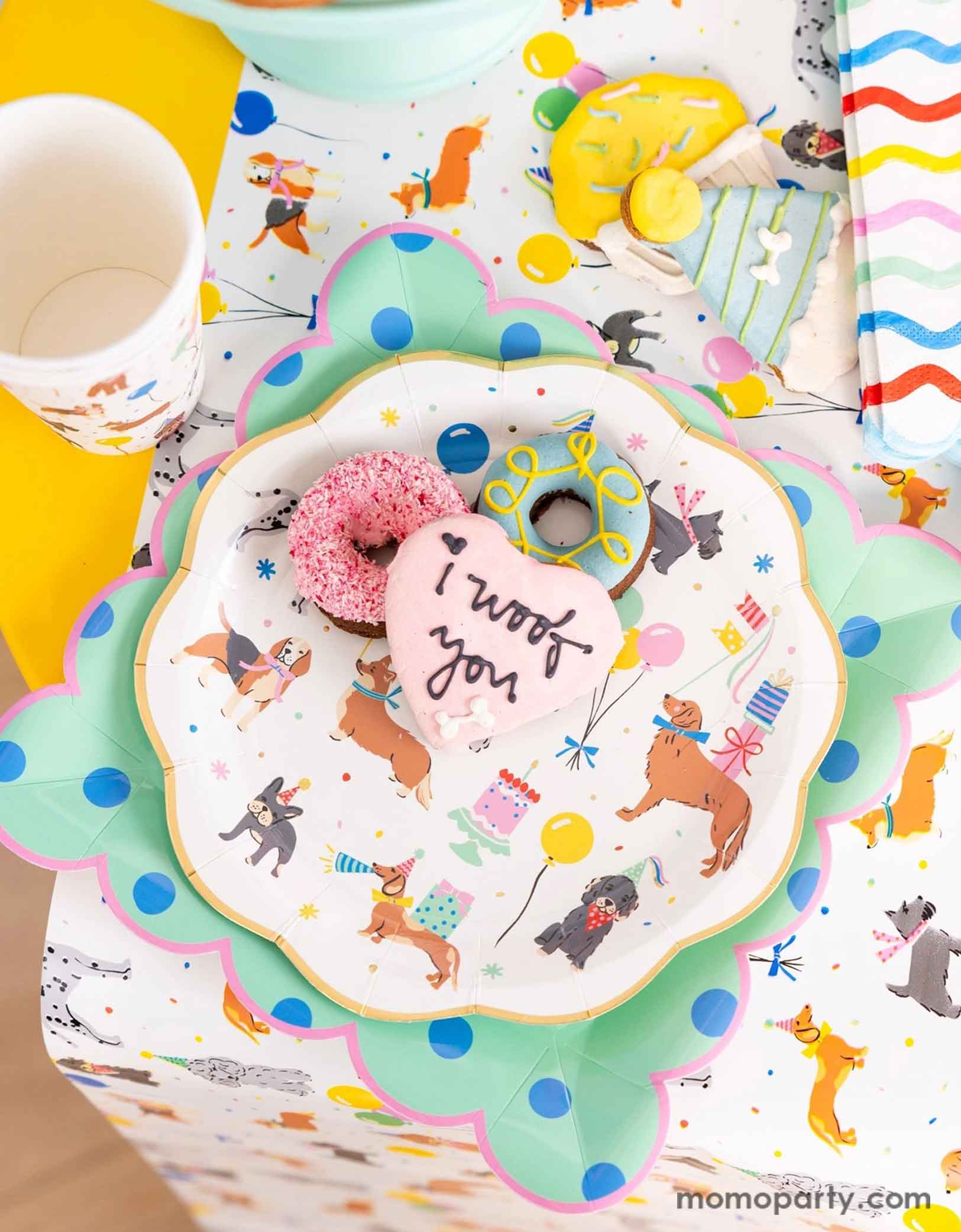 A festive and cheerful dog themed party table featuring Momo Party's dog party tableware collection including dog paper plates, party cups, napkins and table runner featuring adorable illustrations of different breeds of dogs with party hats, balloons and birthday cakes. With mint polka dot square plates and birthday festive sugar coated cookies that say "I Woof You" this  table is ready for a fun and playful birthday celebration for a pet lover!