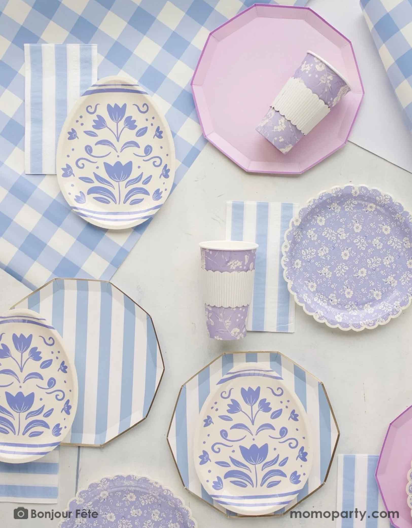 A beautiful Easter party tablescape featuring Momo Party's Easter themed party supplies in light blue and lilac including sky blue cabana striped dinner plates, napkins, floral egg shaped plates, blue ditsy floral scallop plates, matching paper cups on n a blue gingham table runner - the perfect party essentials for an elegant Easter celebration.