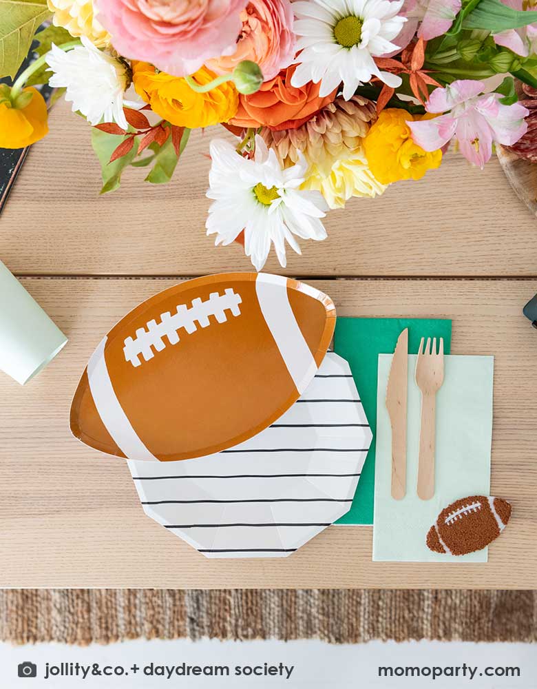 A modern football party table filled with Momo Party's football themed party tableware by Daydream Society including the die-cut football shaped plate, black striped plate with green and mint napkins and party cups. In the center of the table there's a beautiful flower bouquet, all makes great inspirations for football themed celebrations, whether it's a kid's football birthday bash, a Super Bowl watching party or a Sunday football viewing party. 