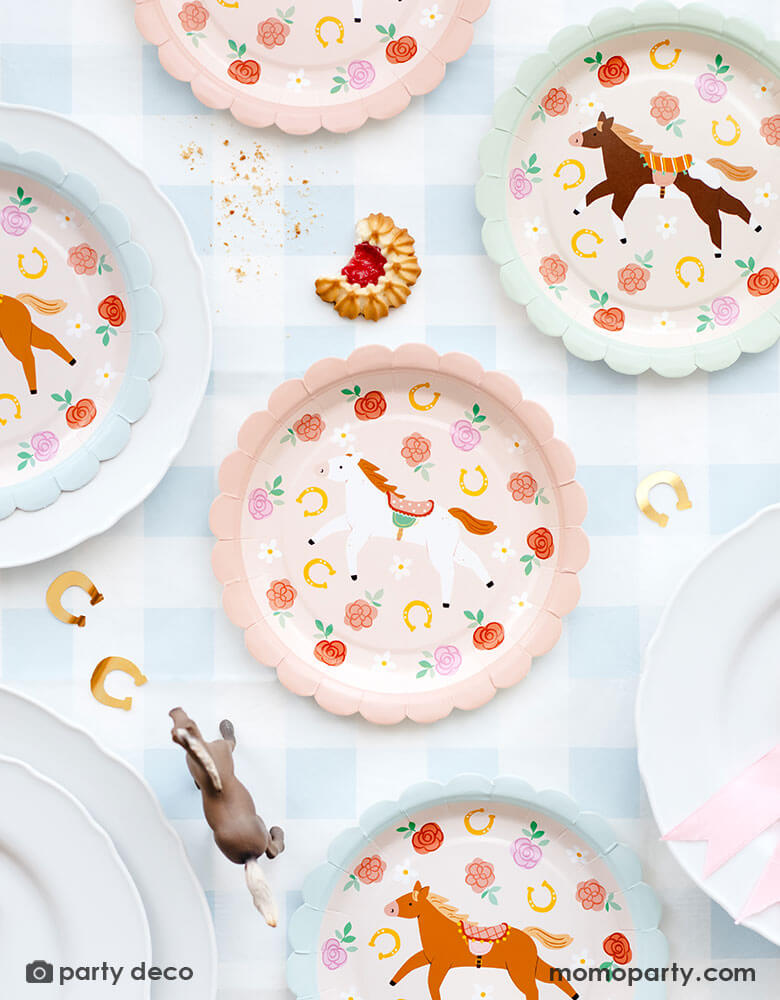 A overhead shot of a party table featuring Momo Party's 7" floral pony paper plates in 3 different colors and designs by Party Deco. The plates are placed on a light blue gingham tablecloth and around the paper plates are some gold horseshoe shaped confetti and some cookies, making this a perfect inspo for girl's pony or horse themed birthday party table decoration idea!