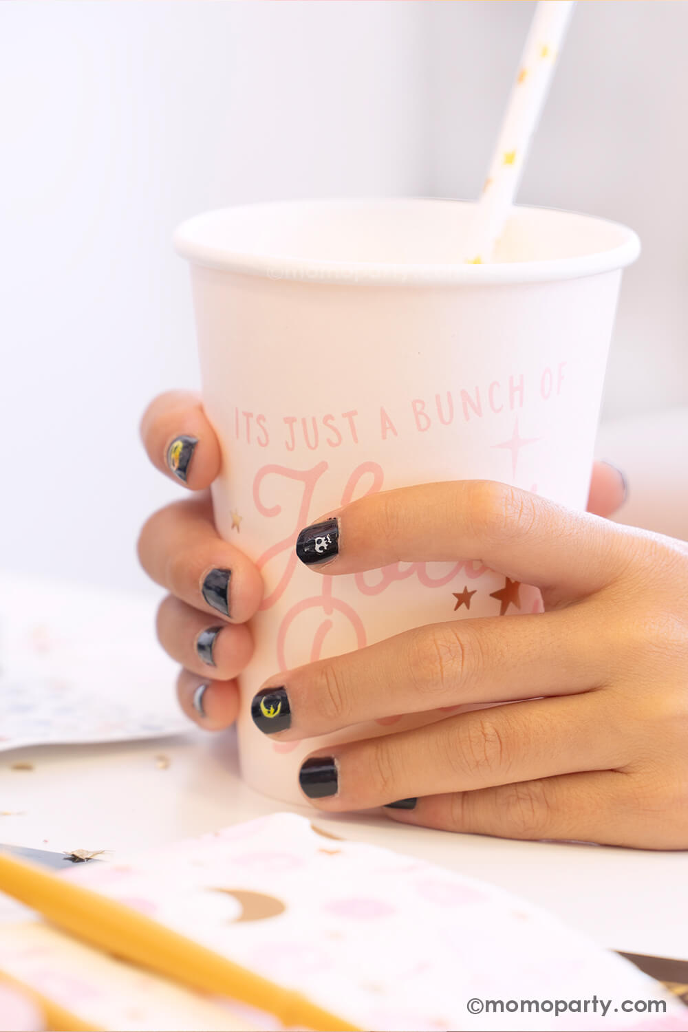 A kid's hand holding Momo Party's Hocus Pocus pink party cup in a witch themed Halloween party. The girl is wearing black nail polish with Halloween themed nail stickers including a crescent moon, a skull, a jack=o-lantern from the Snails Nail Polish Halloween Spooky Pack - which makes a perfect party favor or activity for kid's Halloween party.