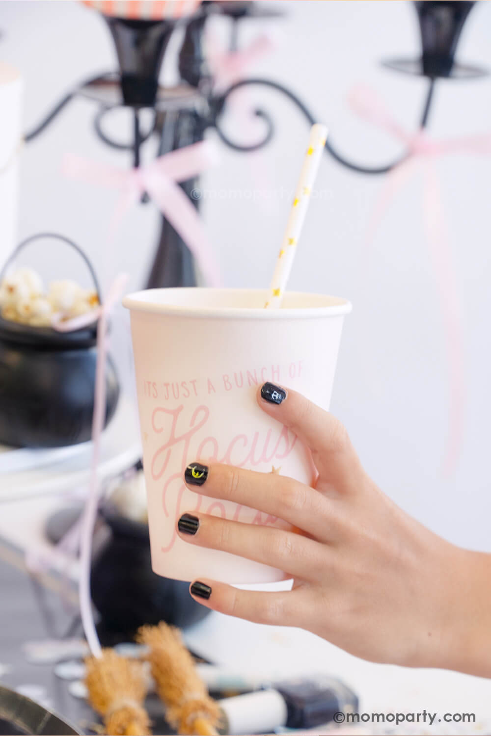 A kid's hand holding Momo Party's Hocus Pocus pink party cup in a witch themed Halloween party. The girl is wearing black nail polish with Halloween themed nail stickers from the Snails Nail Polish Halloween Spooky Pack - which makes a perfect party favor or activity for kid's Halloween party.