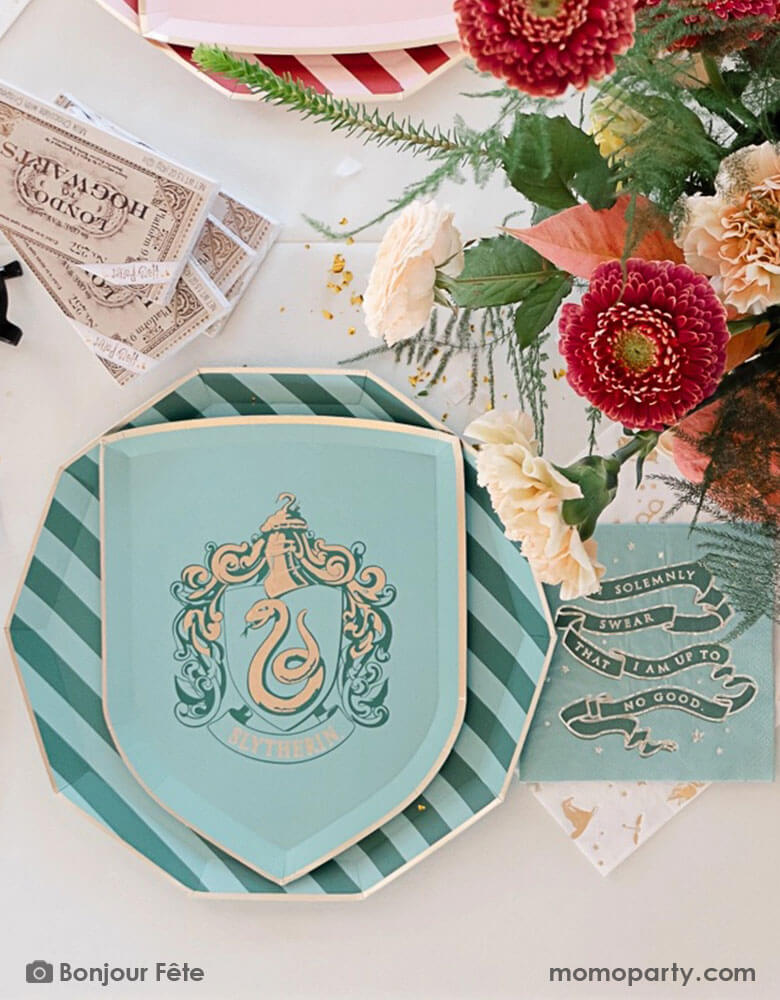 A beautiful and elegant Harry Potter themed party tablescape features Momo Party's Harry Potter house pride shield-shaped 7" side plate with Slytherin logo and color paired with 10.25 green striped dinner plate. Next to the plates are Harry Potter motif large napkins in gold foil and Slytherin green small napkins. On the table are some tickets Hogwarts and pretty flower arrangement - making this a great inspo for a modern Harry Potter themed birthday party celebration.