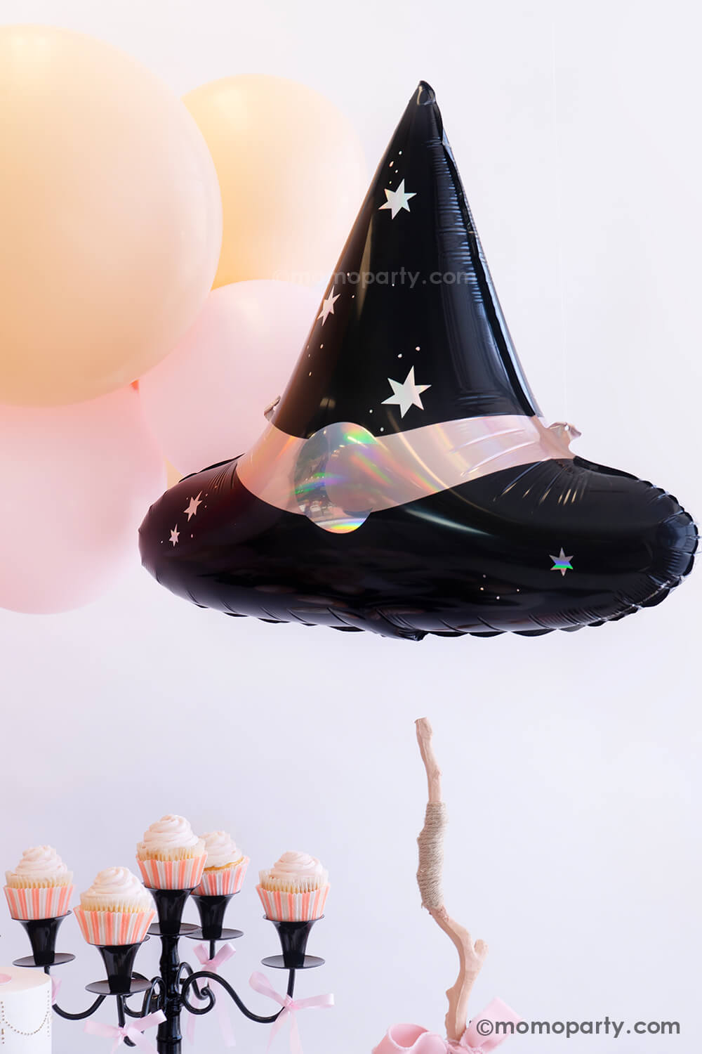 Momo Party's 23.5 x 19 inches Hocus Pocus witch hat shaped foil balloon by Party Deco hung next to a pink balloon cloud as the decoration for an adorable pink Halloween party. On the table there are pink cupcakes on a black candle holder which is adorn with pink ribbons with a touch of elegance and sweetness for a fun and kid's friendly Halloween celebration.