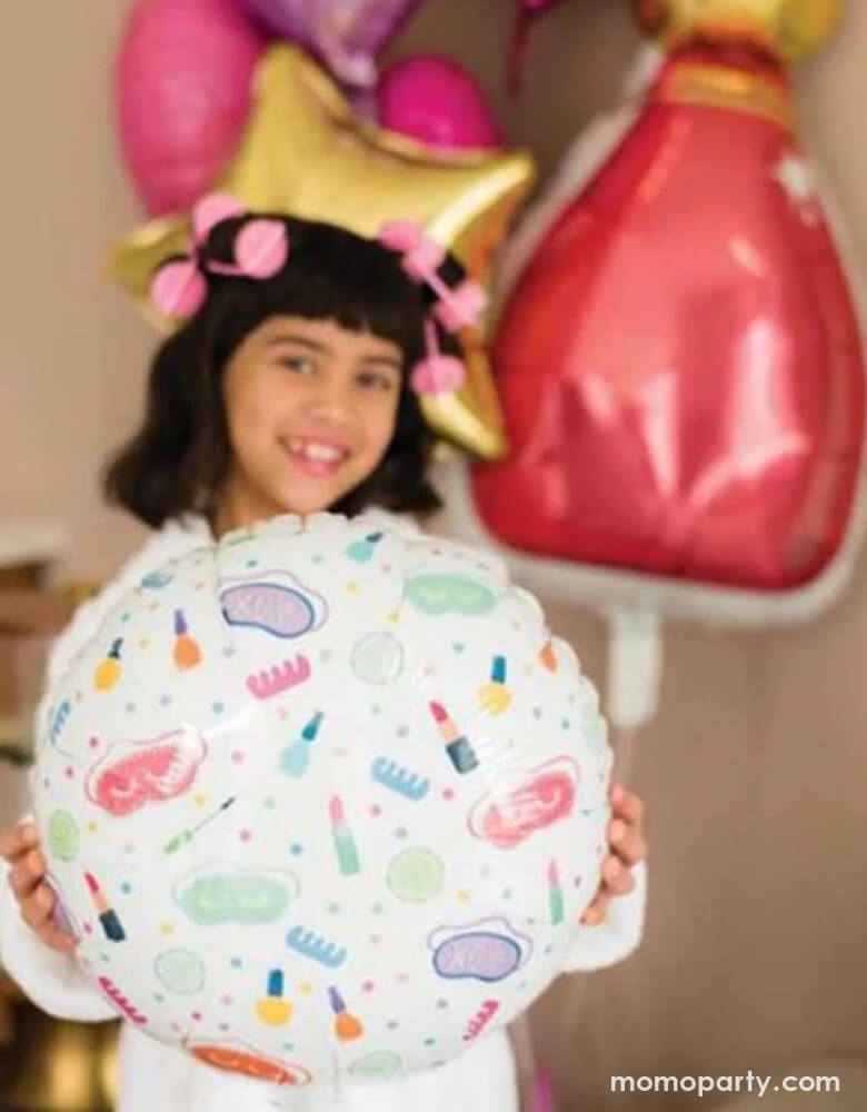 A school aged girl in her robe and hair curls holding Momo Party's 18" spa party round foil balloon by Anagram Balloons. In the back there are some colorful birthday party balloons including a nail polish bottle shaped foil balloon, some star shaped balloons in gold, pink and purple - a fun party decoration for girl's sleepover or slumber parties!