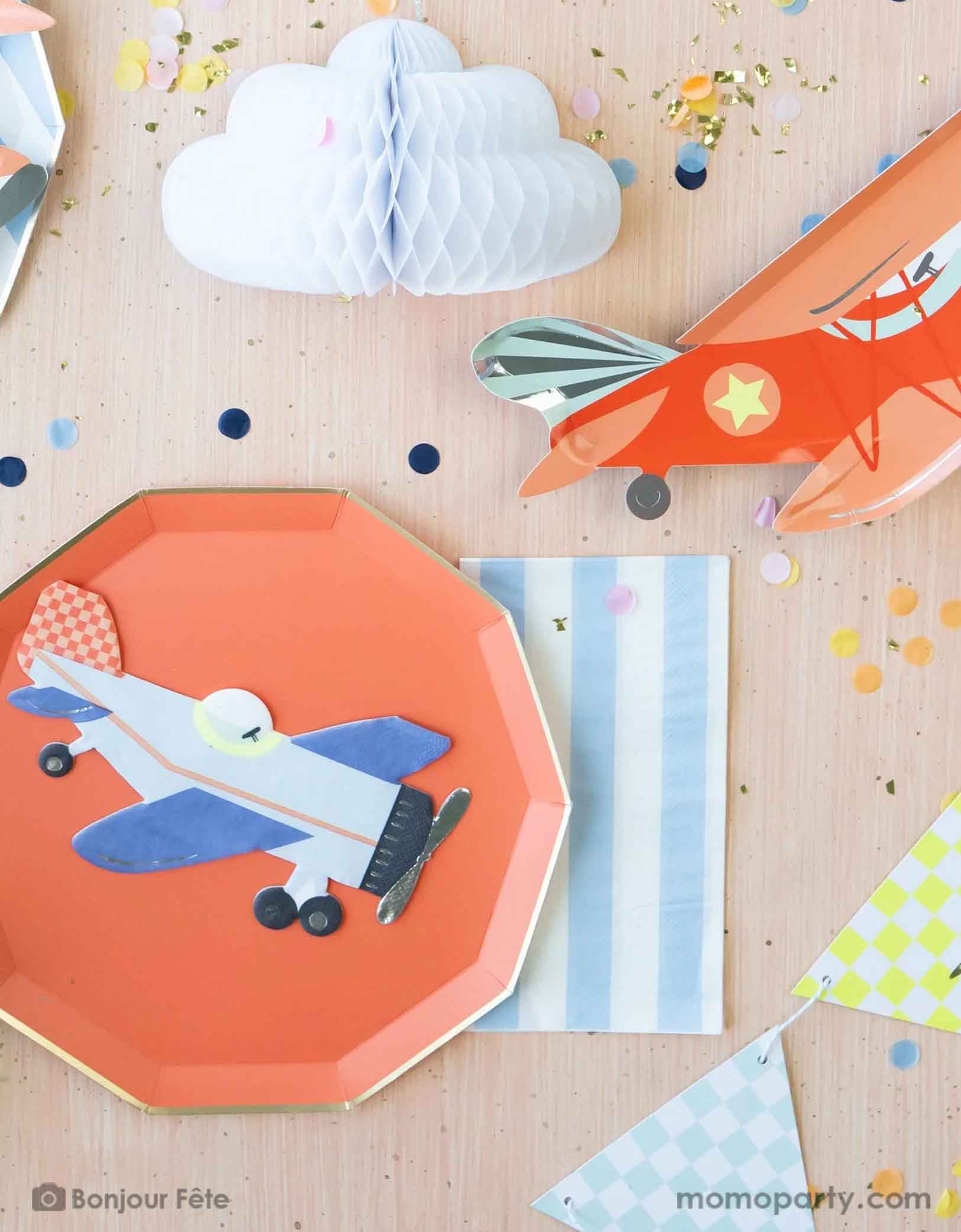 A kid's airplane themed birthday party tablescape featuring Momo Party's plane themed party supplies including Meri Meri's vintage airplane shaped napkin, plate and party garland pennants. A cabana inspired striped sky blue guest napkin is paired with the red decagon plate with gold foil edge. On the table there's an adorable honeycomb cloud and some festive confetti, making this a perfect inspiration for a modern and cute table setting idea for a boy's birthday party.