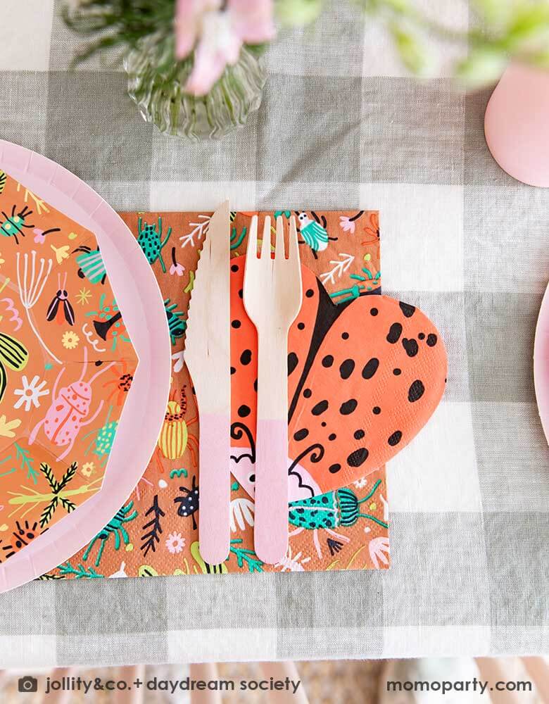 A close up shot of a cute kid's bug insect themed party table set up featuring Momo Party's backyard bug patterned plates, napkins paired with pink party cups, cutlery set and plates. With an olive green gingham tablecloth under and a beautiful flower bouquet, this makes a perfect inspiration for a modern take of a kid's bug themed celebration.