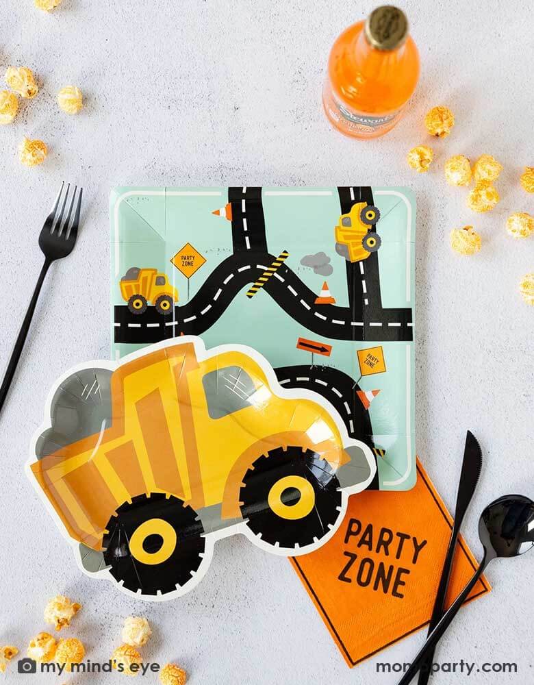 A kid's construction themed party tablescape featuring Momo Party's construction themed party supplies including the square truck road plate, the truck shaped plate, a party zone napkin, black cutlery, orange soda bottle and some popcorn around. Making this a perfect inspo for a kid's festive construction themed birthday party.
