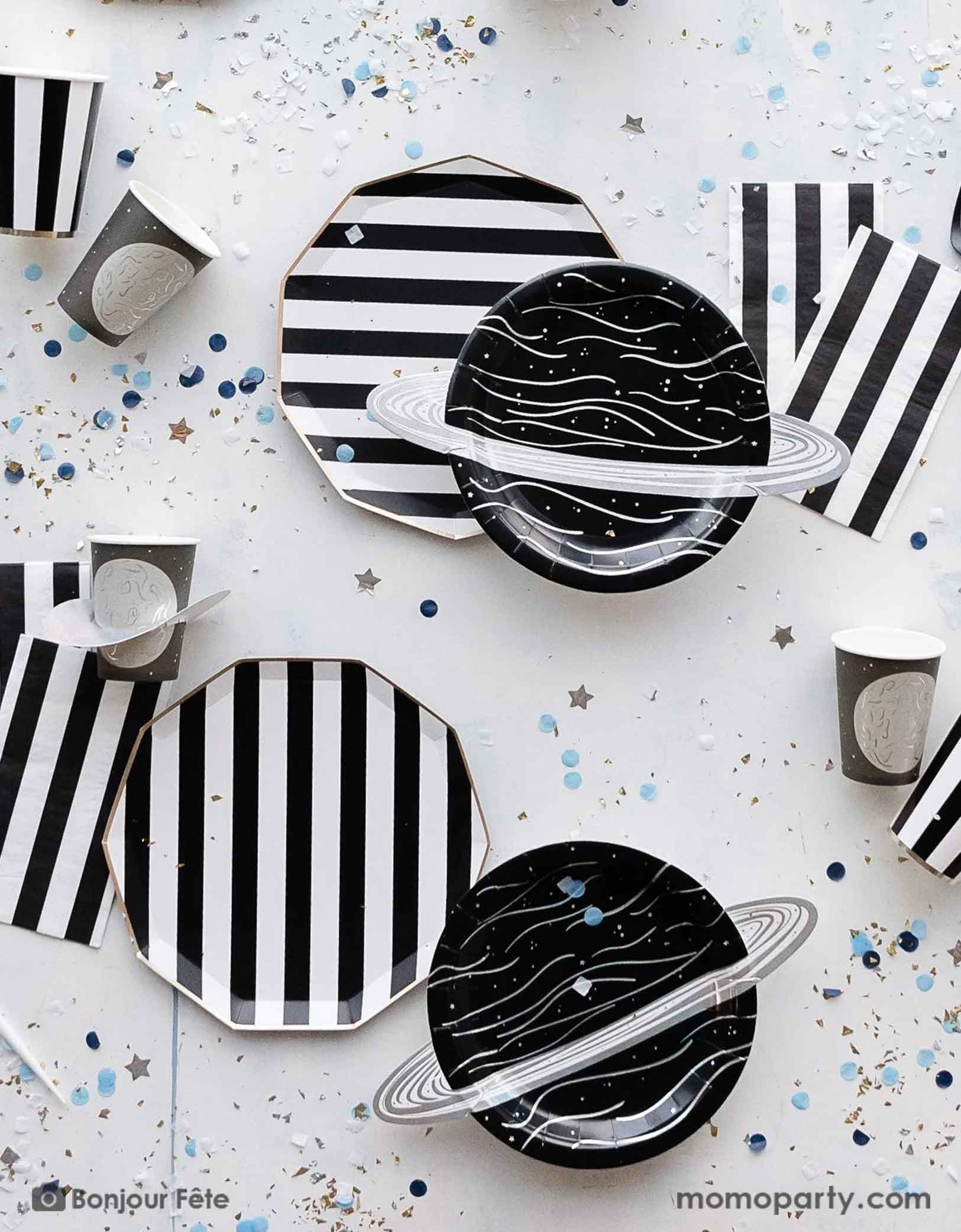 A space themed party table featuring Momo Party's Black Striped Party Supplies including paper dinner plates, guest towels, black and white cutlery set. With the planet 3D party cup, planet shaped plates and metallic star confetti around the table, this makes a perfect inspo for a chic, stylish and modern space themed celebration.