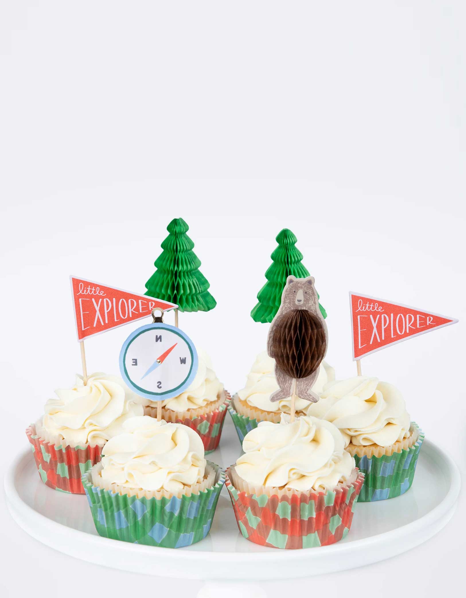 A few cupcakes decorated with Momo Party's Camping Adventure Cupcake Kit by Meri Meri. Create a cupcake centerpiece for your camping adventure party, or hand them out to hungry little explorers as a sweet treat. This kit is beautifully presented in a camper van style box. 24 cupcake toppers in 4 designs, including honeycomb bears, honeycomb trees, compasses and explorer flags, with shiny gold foil details.