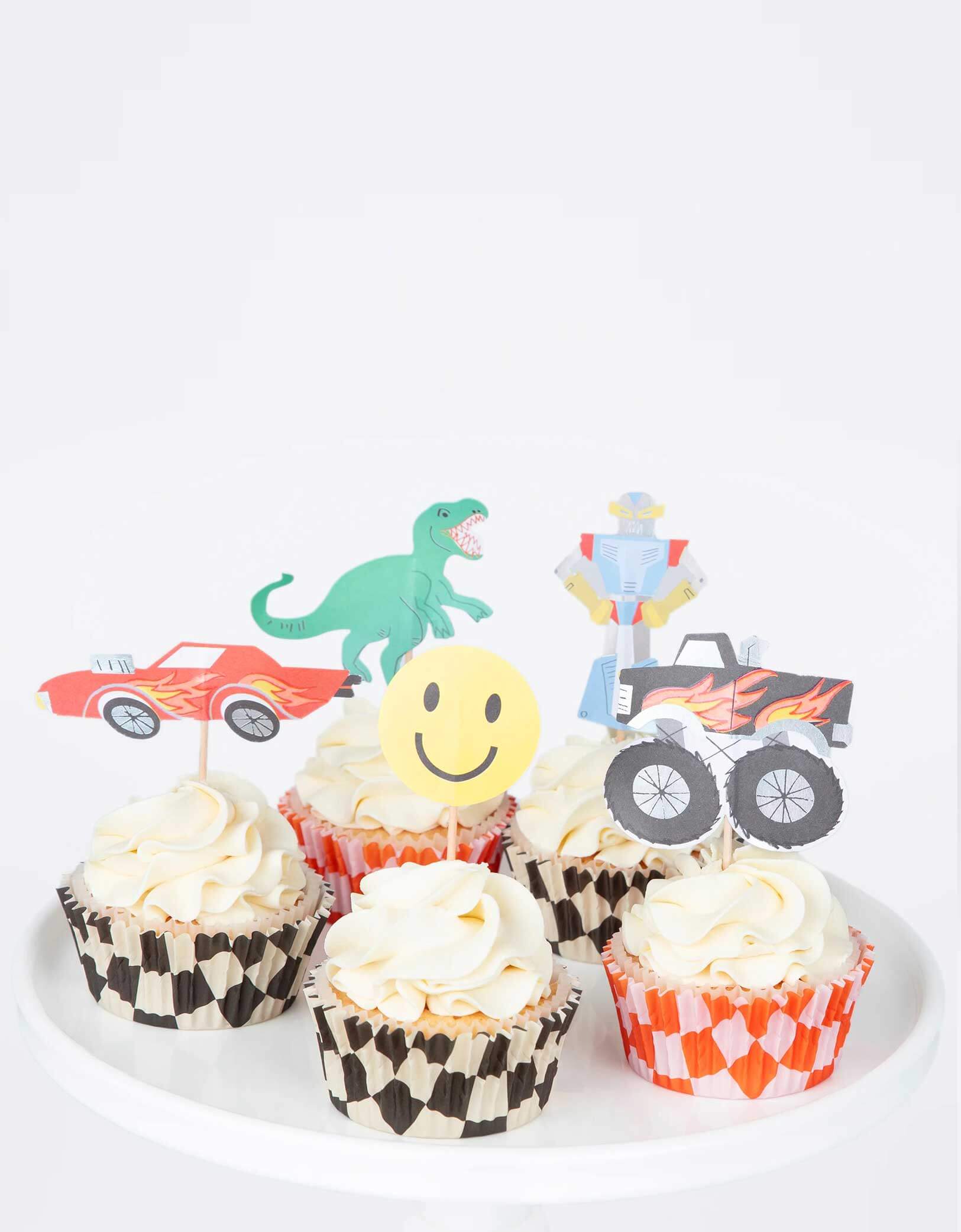 A few cupcakes decorated with Momo Party's Monster Truck Cupcake Kit by Meri Meri, featuring iconic retro toy cupcake toppers, including 5 designs of a monster truck, a car, a robot, a T-rex and a smiley face and checked cupcake cases, to make the most fun and tasty treats. This fun kit also makes a great gift for kids who love to bake.