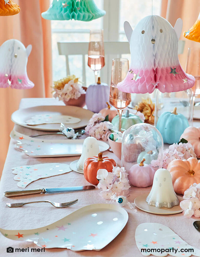 A festive pastel themed Halloween party table decoration featuring Momo Party's ghost with pastel stars plates and napkins by Meri Meri. On the table three are pastel colored pumpkins, autumn flower arrangement and ghost shaped candles are the centerpiece, along with Meri Meri's honeycomb ghost hanging decorations dipped with pastel colors and silver foil stars, this soft and sweet set up makes a great inspo for a kid's non-scary halloween party decorating ideas!