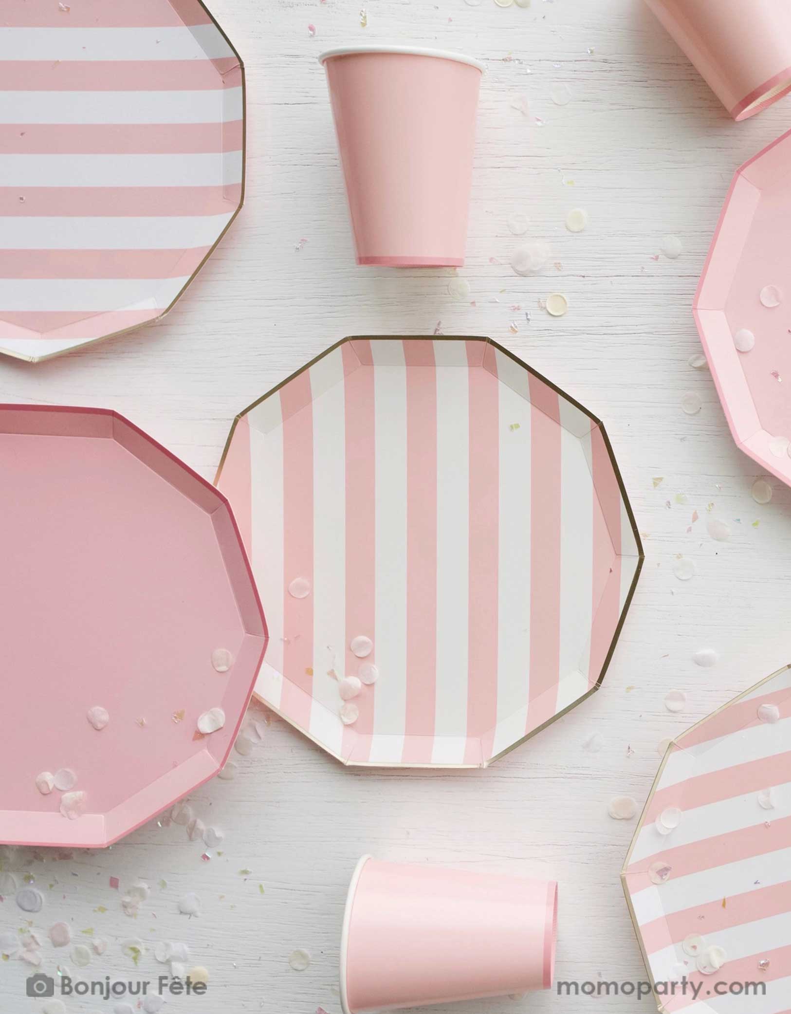 An overhead shot of a party table filled with Momo Party's pastel pink themed party tableware including pastel pink cabana striped dinner plates and pastel pink dinner plates in decagon shape with matching party cups, with pale pink confetti - a great collection for girl's birthday or a baby girl shower. 