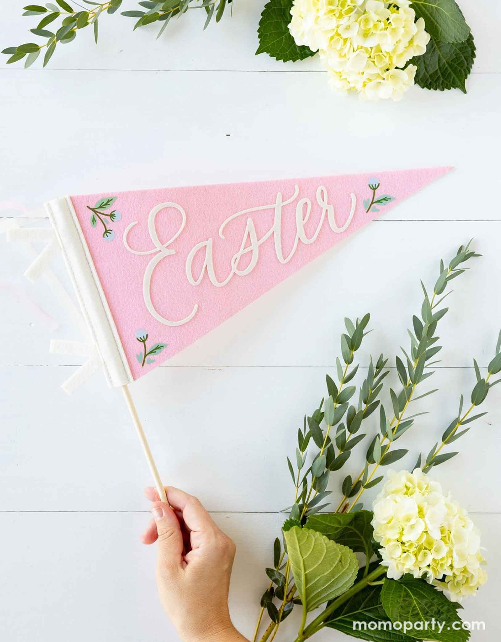 A lady's hand holding Momo Party's 15" pink felt pennant banner features the words "Easter" in fun, playful letters. Around the pennant there are some spring floral bouquet, a perfect inspiration for spring or Easter celebration!