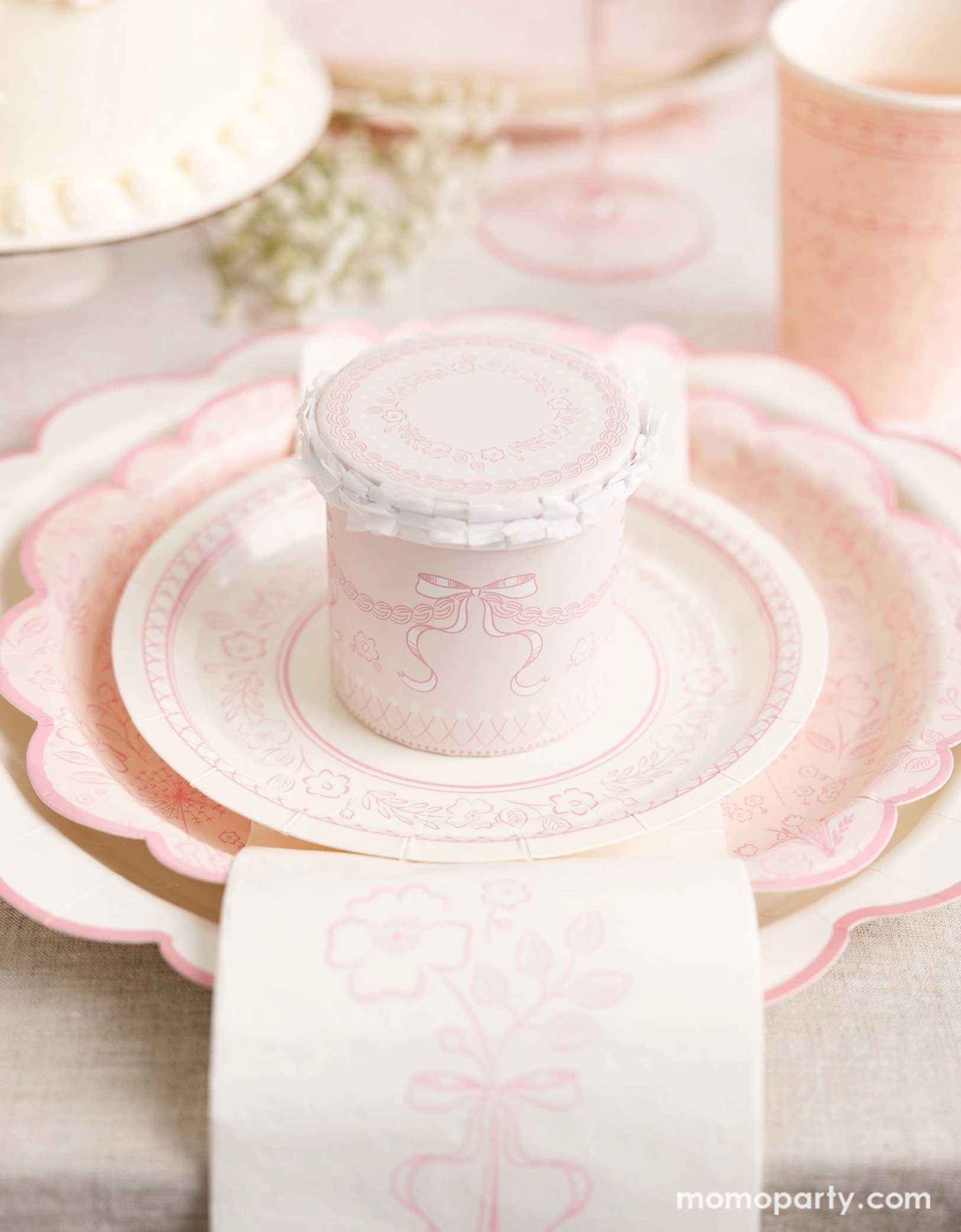 An elegant placeset featuring Momo Party's Pink Pembroke tableware collection including the 12" Pembroke Pink Edge Scallop Plate paired, 9" Pembroke Pink floral Plate, 7" Pembroke Pink Plate, the Pembroke Pink napkin and the matching party cup. With a pretty floral arrangement, a pink buttercream cake and a pink champagne glass in the back, this table setting is perfect for a spring inspired celebration, be it an Easter celebration or Mother's Day party.