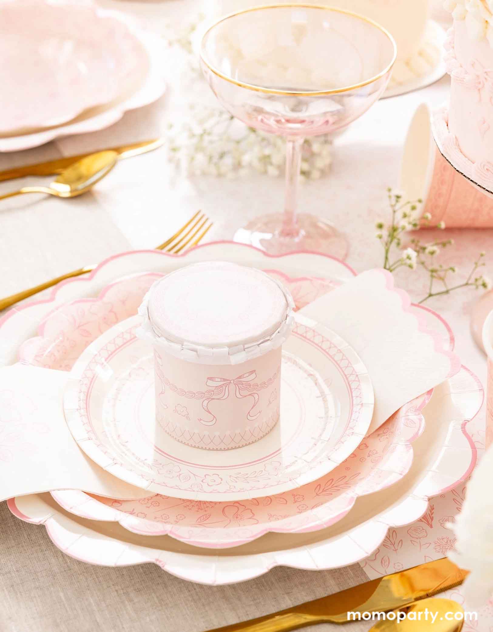 An elegant placeset featuring Momo Party's Pink Pembroke tableware collection including the 12" Pembroke Pink Edge Scallop Plate paired, 9" Pembroke Pink floral Plate, 7" Pembroke Pink Plate, Pembroke Pink napkin and the matching party cup. With the gold foil utensil set, a pretty floral arrangement and a pink champagne glass, this table setting is perfect for an Easter celebration or Mother's Day party.