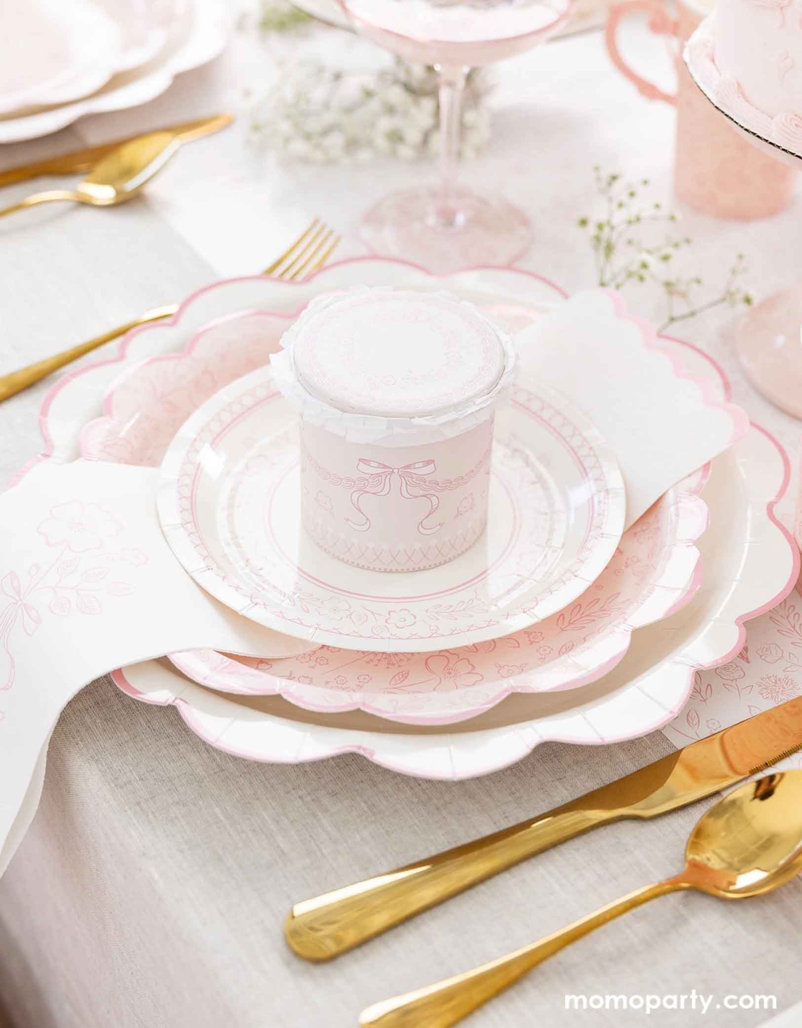 An elegant placeset featuring Momo Party's Pink Pembroke tableware collection including the 12" Pembroke Pink Edge Scallop Plate paired, 9" Pembroke Pink floral Plate, 7" Pembroke Pink Plate, Pembroke Pink napkin and the matching party cup. With the gold foil utensil set, a pretty floral arrangement and a pink champagne glass, this table setting is perfect for an Easter celebration or Mother's Day party.