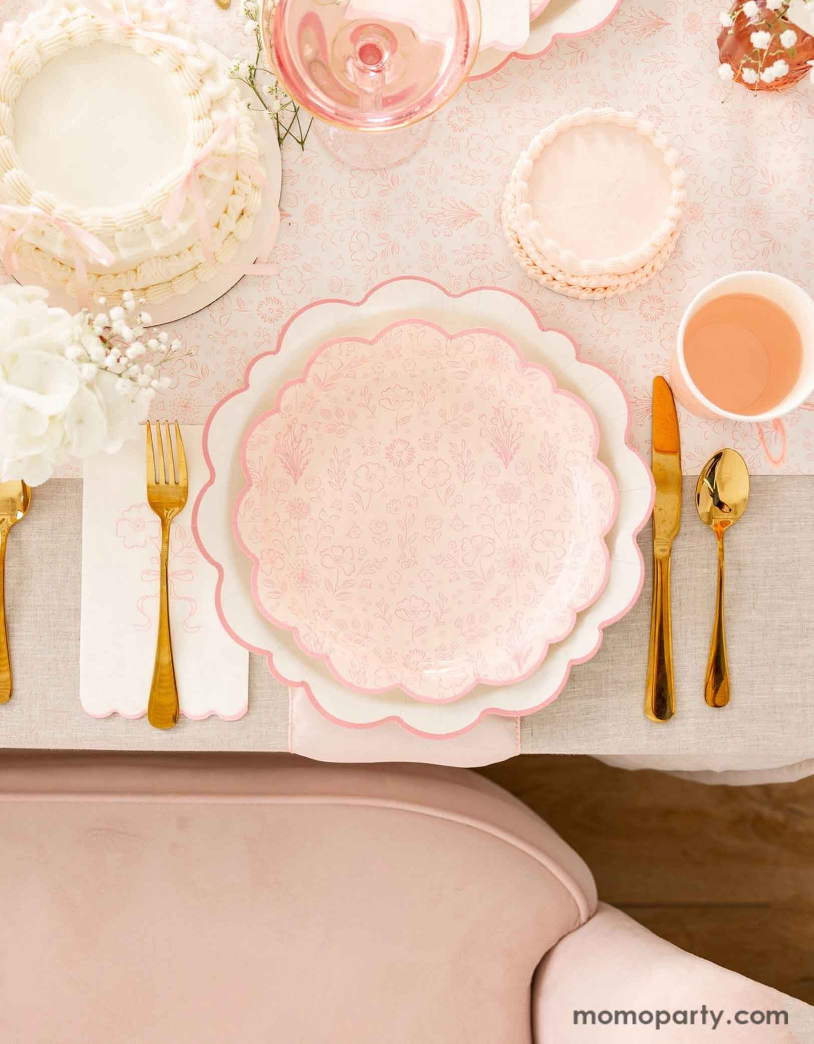 A beautiful and elegant tablescape featuring Momo Party's Pink Pembroke tableware collection including the 12" Pembroke Pink Edge Scallop Plate paired with 9" Pembroke Pink floral Plate and Pembroke Pink Edge Scallop Napkin. Underneath the plates is the Pembroke Pink floral paper table runner. With the gold foil utensil set, a pretty floral arrangement and pastel pink butter cakes and a glass of rose champagne, this table setting is perfect for a spring inspired celebration, be it Easter or Mother's Day.