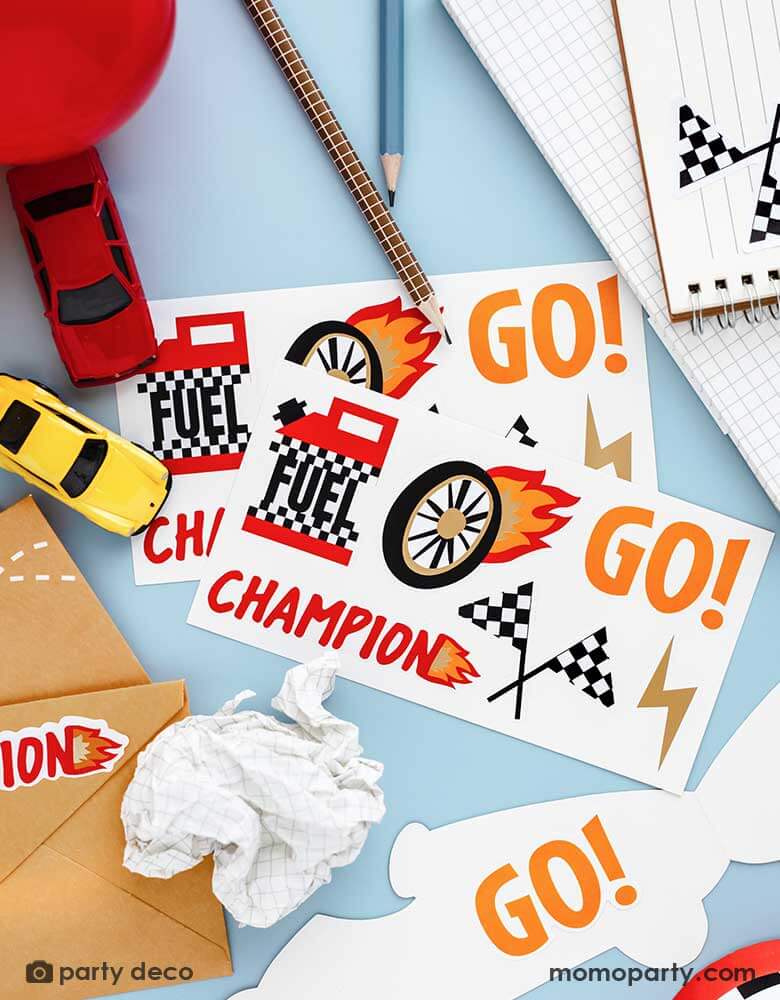 Two sets of Momo Party's race car stickers by Party Deco surrounded by some stationary and toy race cars, the notebook and the party invitations are adorned with these race car themed stickers, making it a perfect idea for kid's race car themed birthday invites.