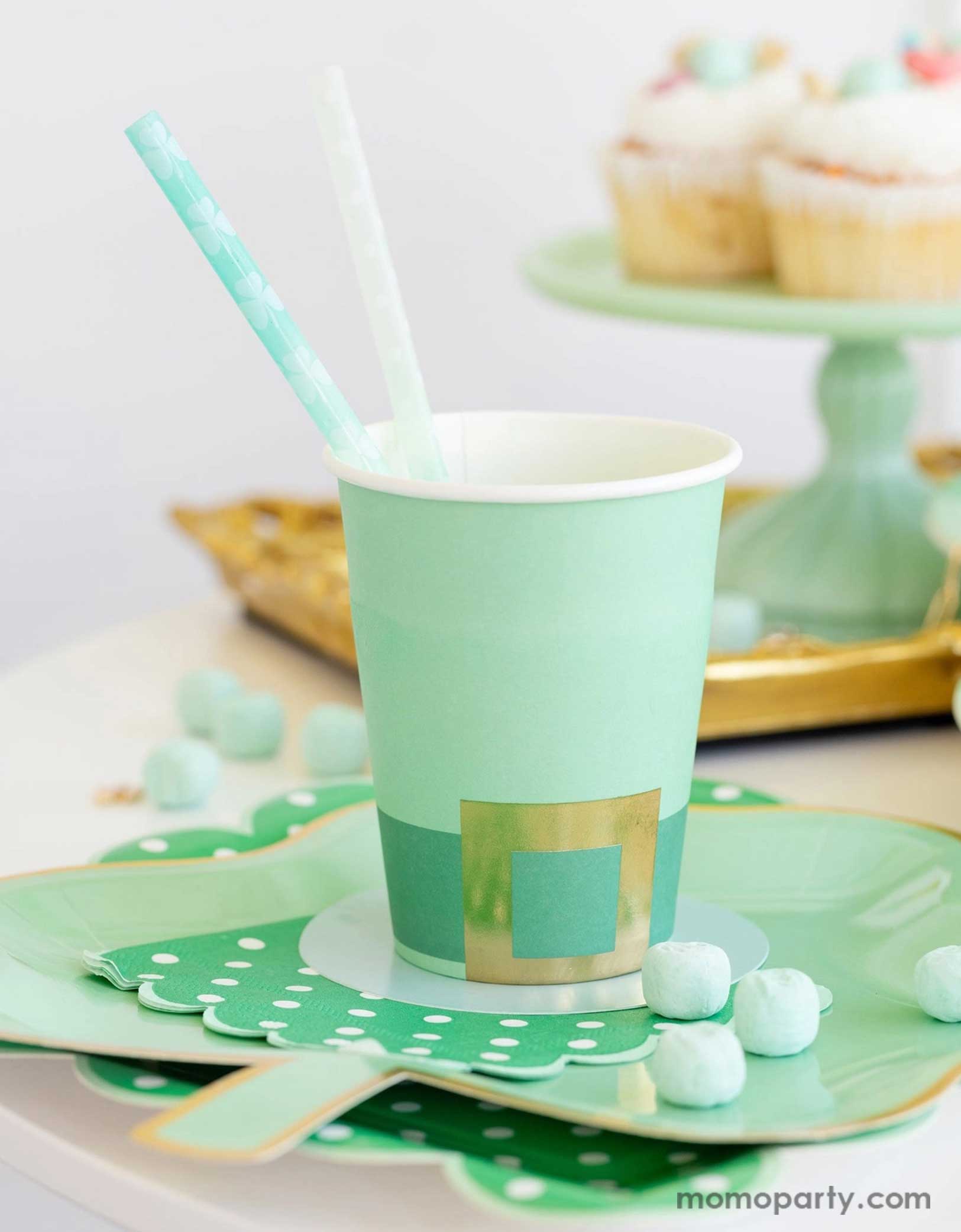 A cheerful St. Patrick's Day party table featuring Momo Party's St. Patrick's Day themed party supplies including the Leprechaun hat party cup, green polka dot napkins, shamrock shaped paper plates, and shamrock reusable straws. In the back there's a green cake stand with cupcakes on a gold serving tray - a great inspo for a fun and festive St. Patrick's Day celebration.