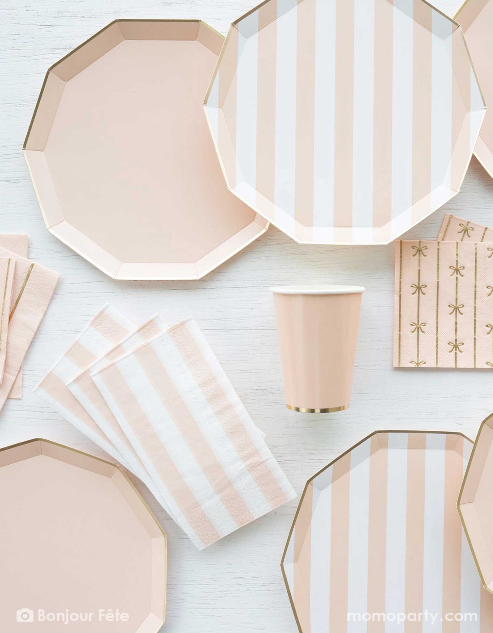 An overhead shot of a party table filled with Momo Party's pastel peach themed party tableware including sweet peach cabana striped decagon dinner plates, napkins and pastel peach dinner plates in decagon shape with matching napkins with bows and party cups - a great collection for girl's birthday, an Easter celebration or a baby girl shower. 