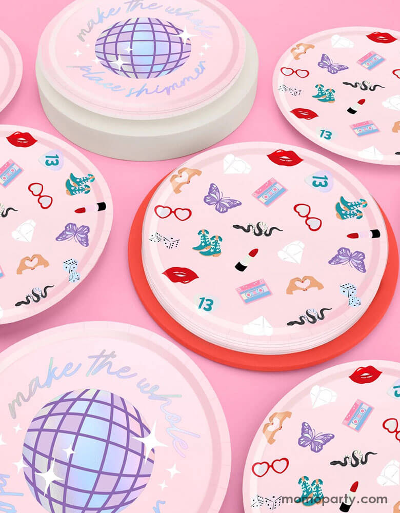 Momo Party's 9" x 9" Taylor Swift Era's Party Paper Plates by Xo, Fetti. Comes in a set of 24 paper plates in two different designs, a disco ball and a Taylor Swift inspired motif featuring red lipstick, red lips, butterflies, cowgirl boots, snakes, cassette tapes, guitar picks, heart hand symbols, and heart shaped sunglasses.  They're perfect for the party table celebrating your Swiftie girl's special day. 