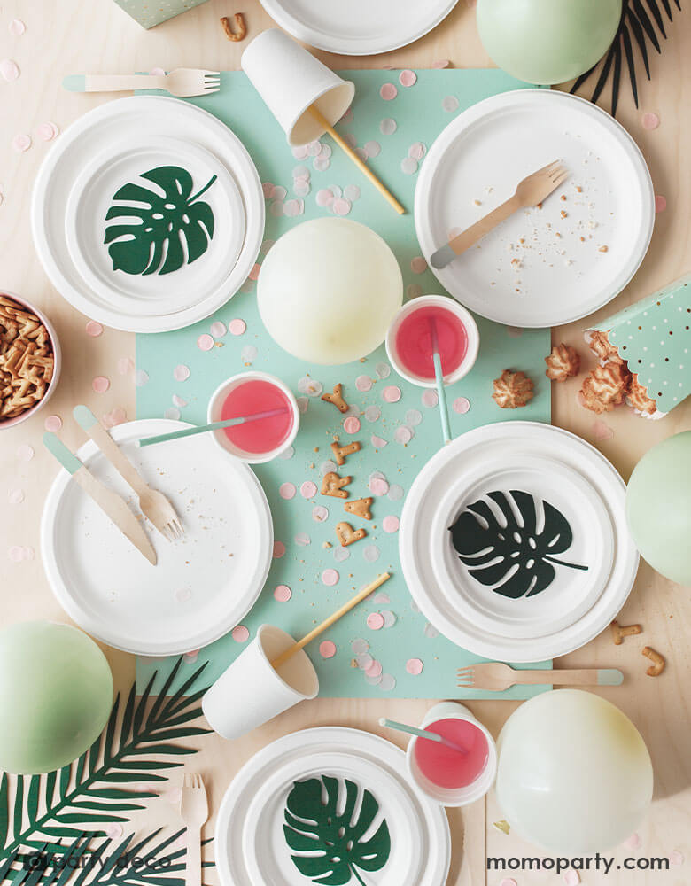 A overhead shot of a tropical themed party table featuring some solid colored tableware adorned with Momo Party's tropical leaves paper decorations in different designs and shades of green. A perfect info for a summer tropical or fiesta themed celebration.