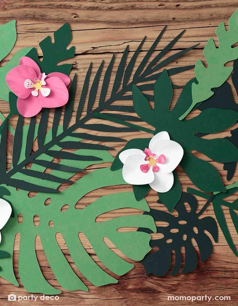 Momo Party's tropical leave paper decorations with some paper flower decorations on a wooden table. These unique tropical leaf decorations contain 21 pieces - &nbsp; 7 different shapes of leaves, each shape in 3 shades of green color. Perfect for a tropical themed birthday party, fiesta or summer garden party.