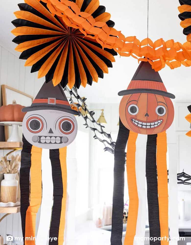 A close-up shot of a modern kitchen that's decorated with vintage inspired Halloween party supplies form Momo Party including the Halloween hanging characters of a skull and a pumpkin, which around them hung the oversized orange and black paper fans and tissue decorations. Making this a eerie yet fun decoration that sets a festive scene for your Halloween celebration this spooky season.