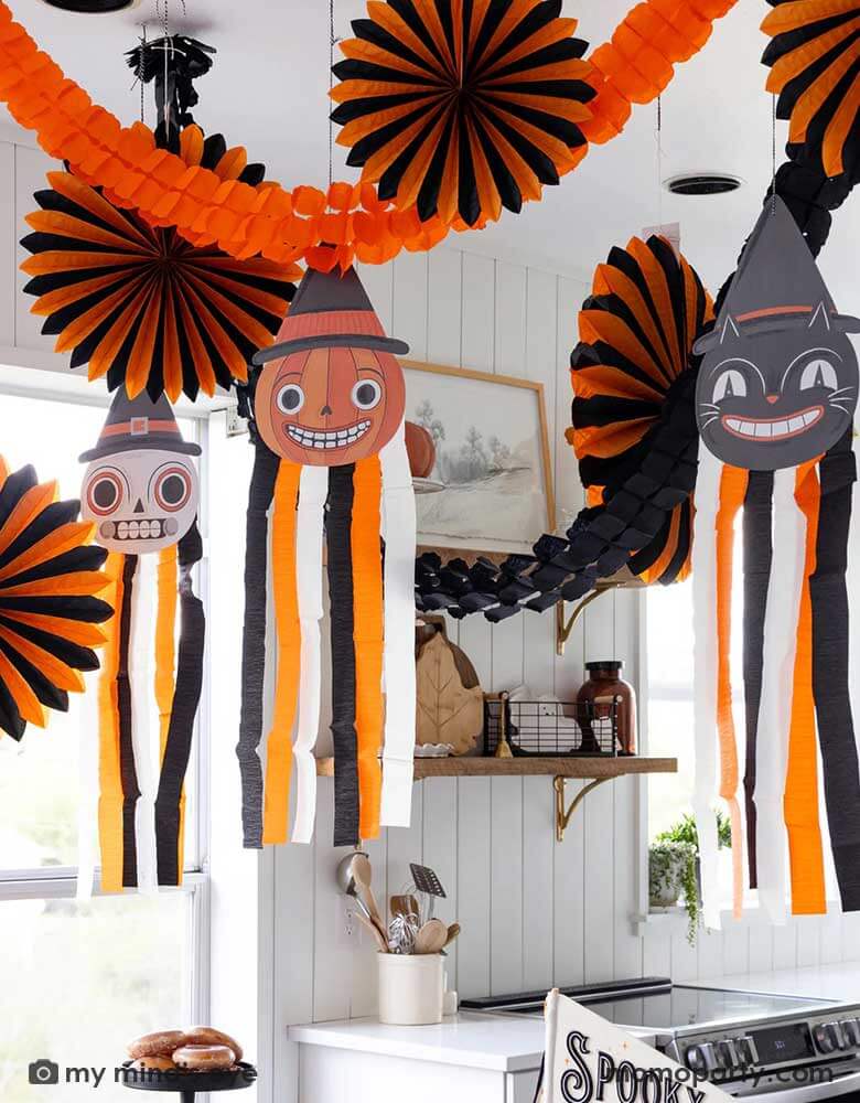 A modern farmhouse kitchen decorated with vintage inspired Halloween party supplies form Momo Party including the Halloween hanging characters of a black cat and a pumpkin, which around them hung the oversized orange and black paper fans and tissue decorations. Making this a eerie yet fun decoration that sets a festive scene for your Halloween celebration this spooky season.