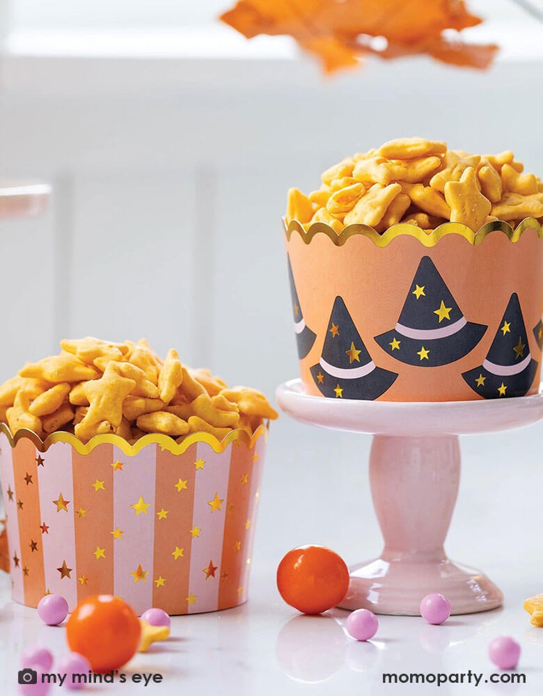 A Halloween party table features Momo Party's Jumbo Witch Hats and Stars Foil Baking Cups by My Mind's Eye. Step up your Halloween party game with these JUMBO foil baking cups featuring witch hats and stars. These 8 oz cups with goldfish, gum balls are perfect for all your spooky treats.