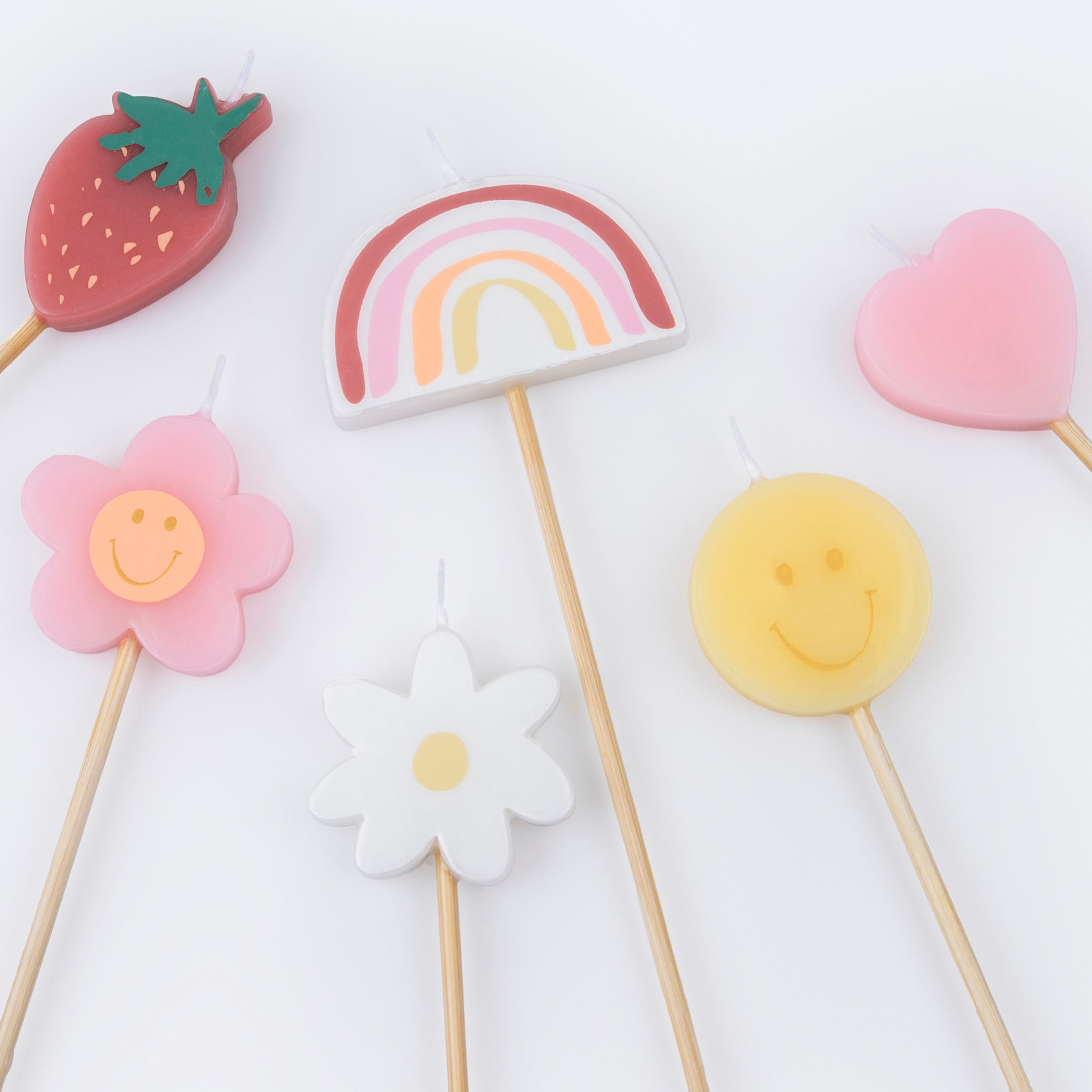 Details of Momo Party's Happy Face Icons Candles by Meri Meri. Featuring a set of 6 strawberry, a flower, a daisy flower, a rainbow, a smiley face, and a heart candle with long sticks, these colorful candles are perfect for any happy celebration!